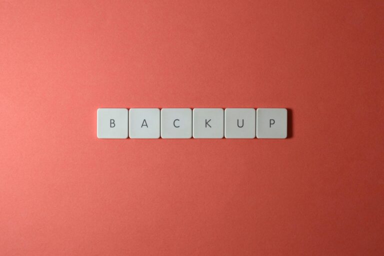 Close-up of keyboard keys spelling 'BACKUP' placed on a coral-colored surface.
